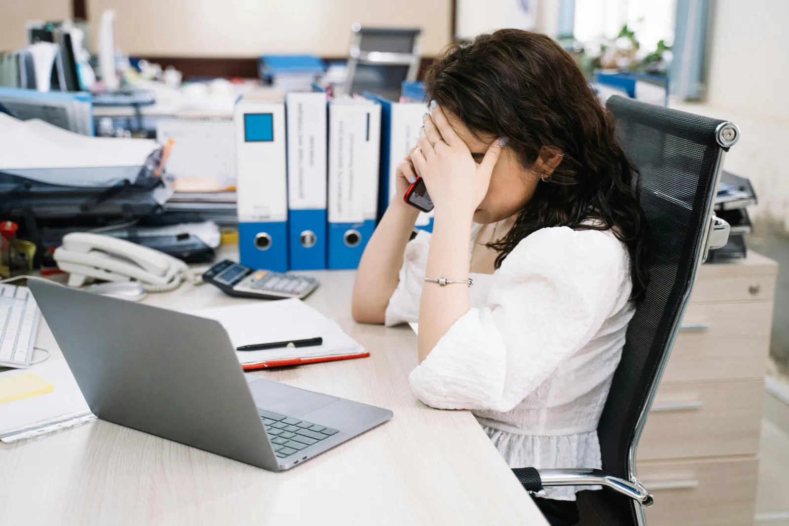 a woman sitting at a desk with a laptop and a phone